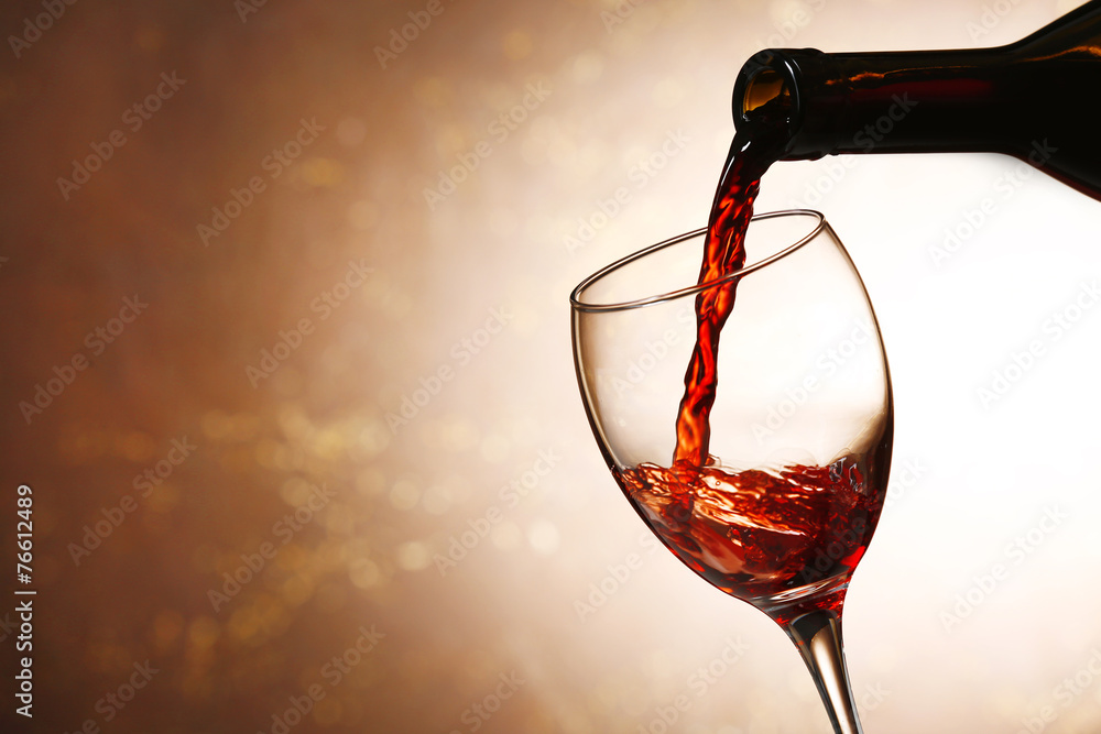 Fototapeta premium Pouring red wine from bottle into glass on color background