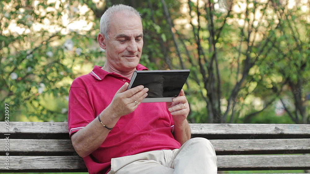 Retired senior man resting and using his tablet at table in park Retired senior man resting and using his tablet at table in park