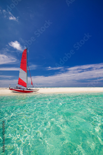 Sailing boat with red sail on beach of tropical island