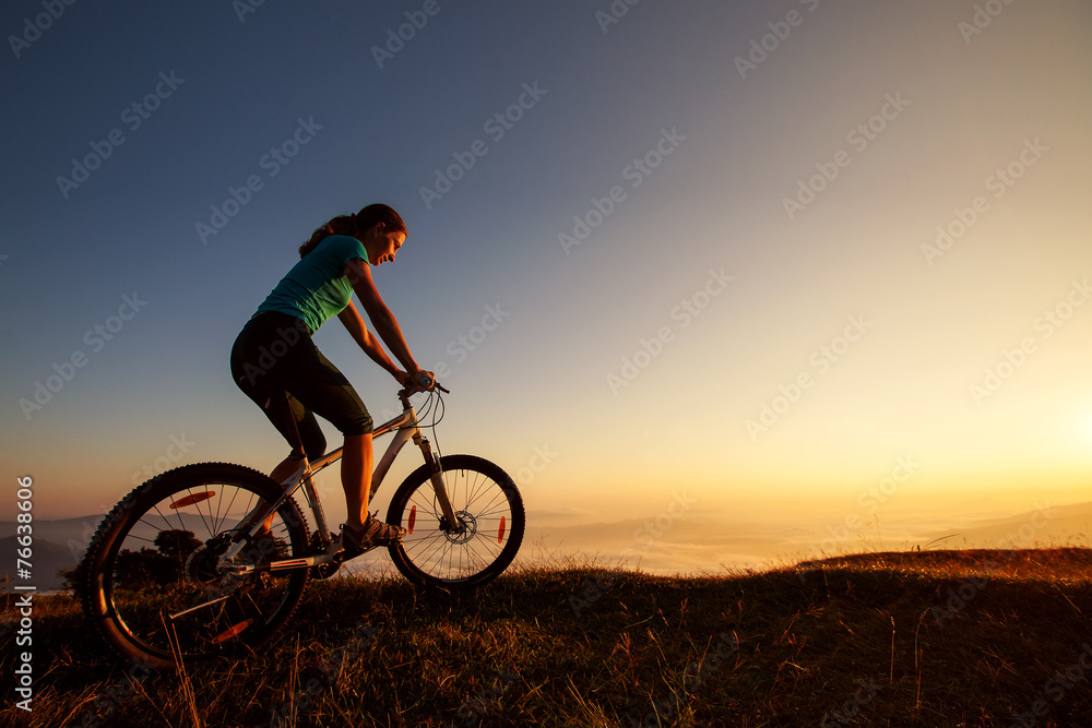 Fototapeta premium Biker-girl at the sunset on mountains