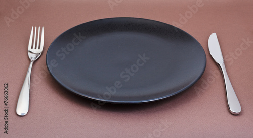 empty black plate with fork and knife on brown
