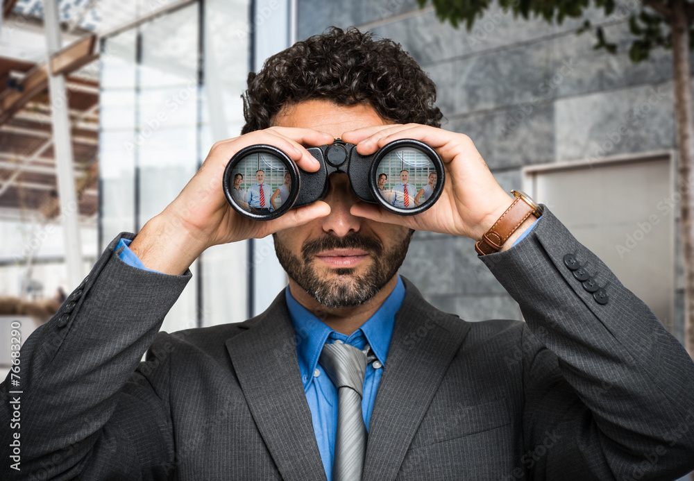 Businessman using binoculars, people portraits in the lens Businessman using binoculars, people portraits in the lens