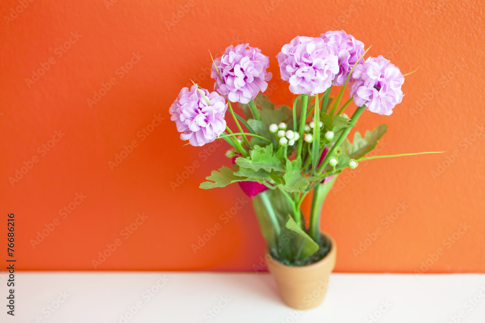 pink artificial flower made from cloth on bright orange wall, wa