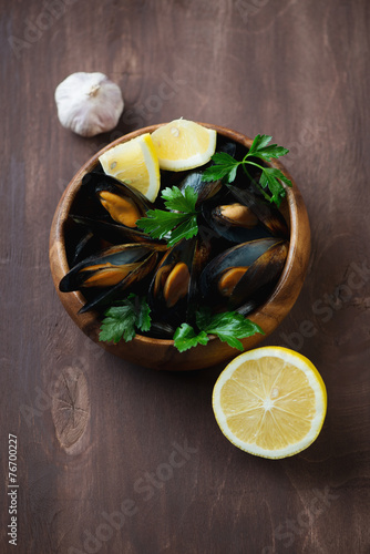 Boiled mussels in a wooden bowl over dark wooden surface