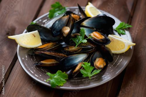 Ceramic plate with boiled mussels over dark wooden background