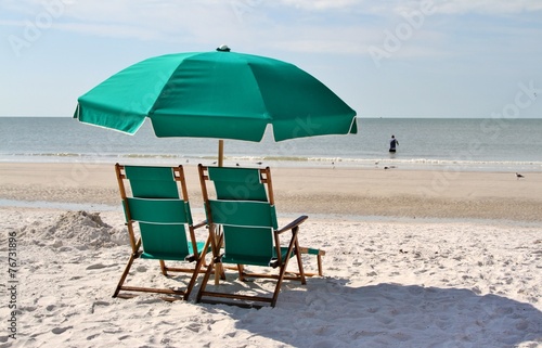 Green sun chairs and umbrella on a beach of an ocean