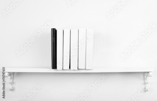 Blank books with black one on bookshelf on white wall