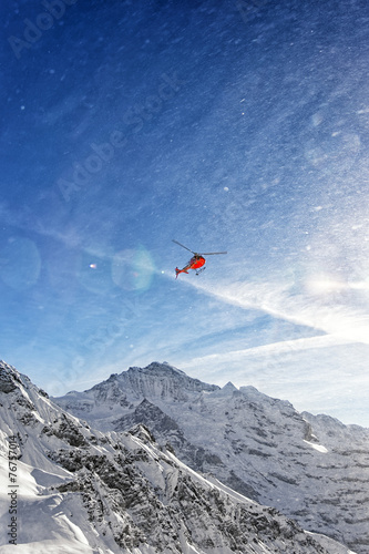 Red helicopter in flight in winter alps with snow powder streams