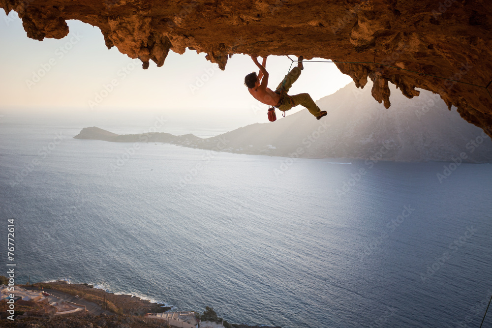 Rock climber climbing along roof in cave at sunset - obrazy, fototapety, plakaty 