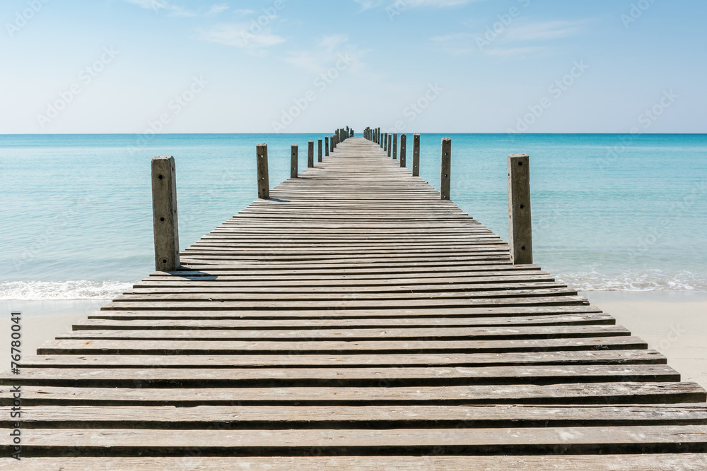 Wooden bridge on the beach to the sea in blue sky.