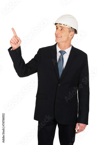 Smiling businessman with hard hat pointing up