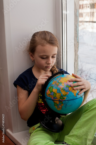 Beautiful little girl sitting near a window. Girl and globe