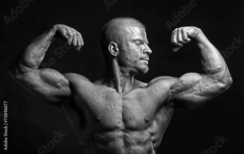The muscular male bodybuilder flexing biceps on black background