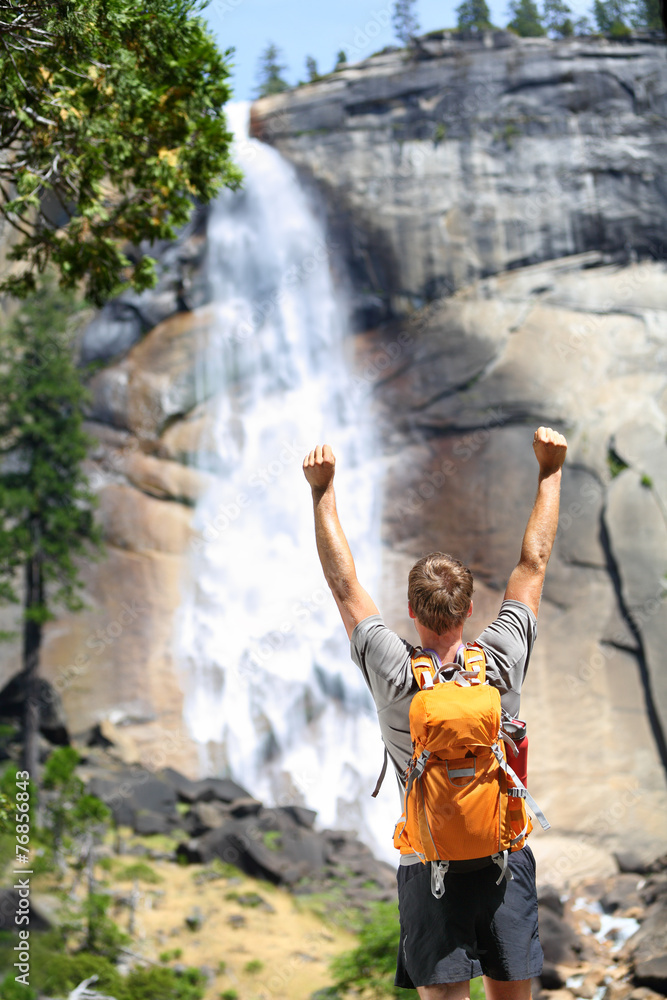 Happy hiking man cheering in success by waterfall