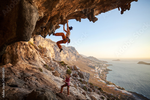 Young woman climbing on cliff, female partner belaying photo