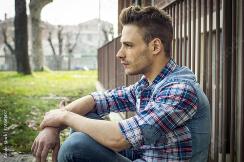 Profile of young man sitting on ground outside