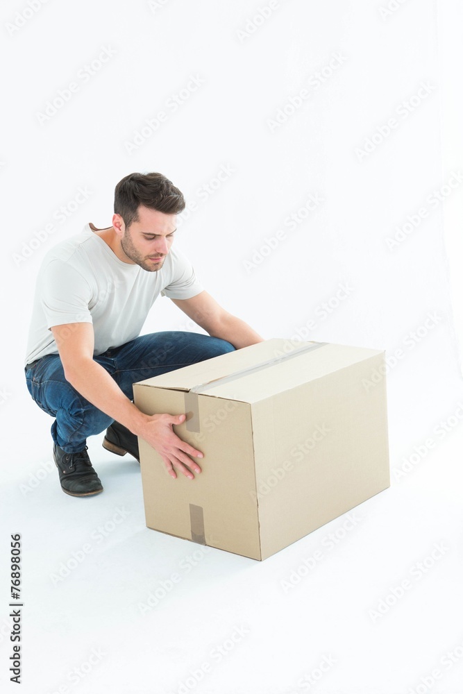 Delivery man crouching while picking cardboard box Delivery man crouching while picking cardboard box