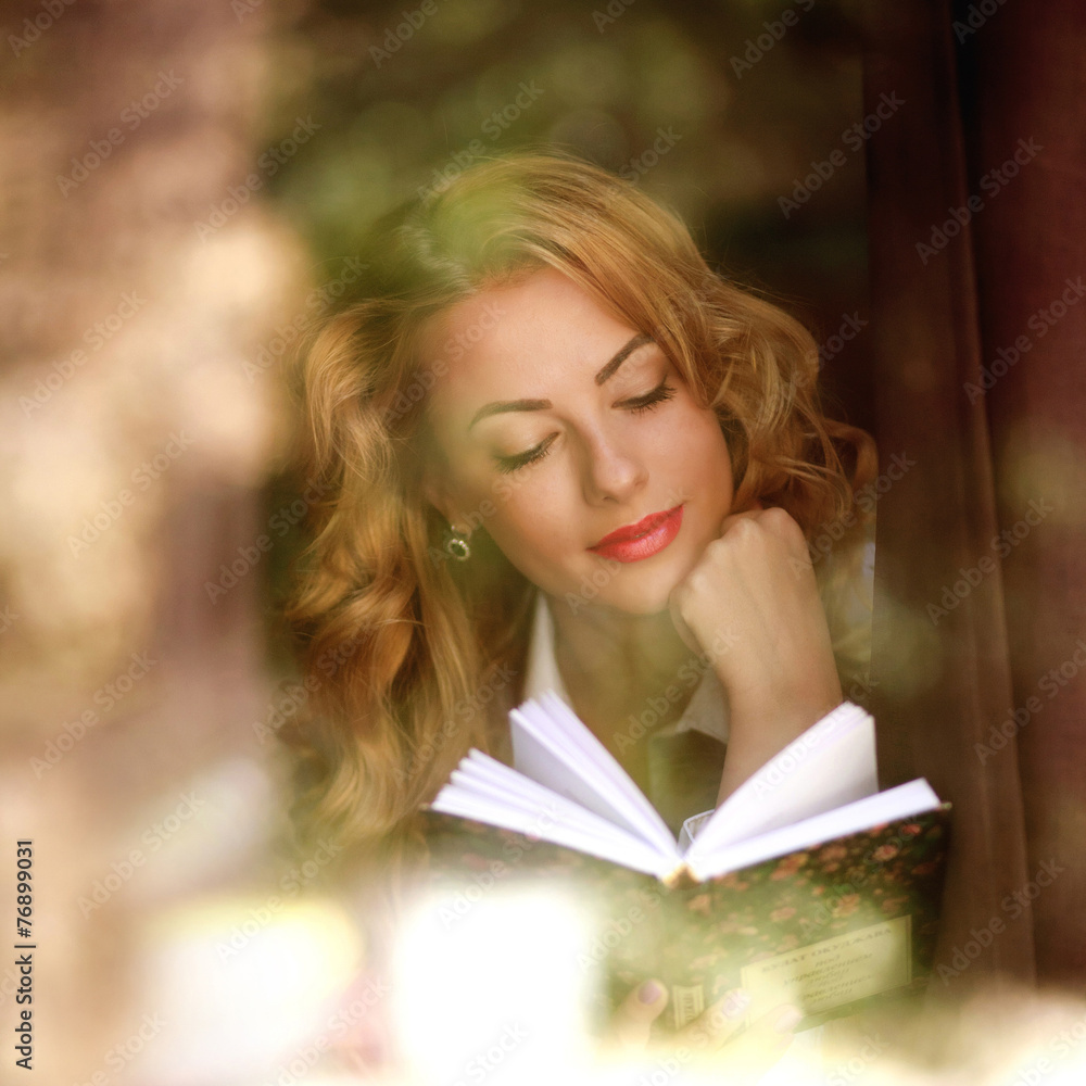 Beautiful girl reading a book indoors, the view through window Beautiful girl reading a book indoors, the view through window