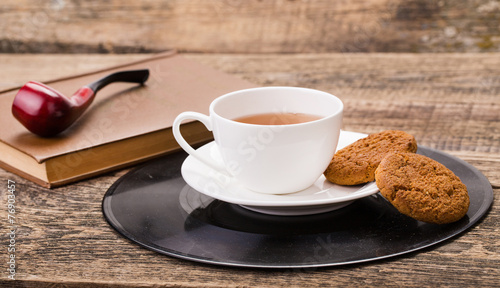 ivory tea cup with sweet cookie  book and tobacco pipe on wooden