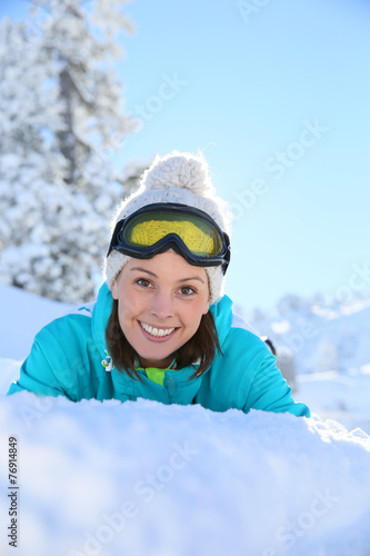 Cheerful girl in ski outfit laying down in snow