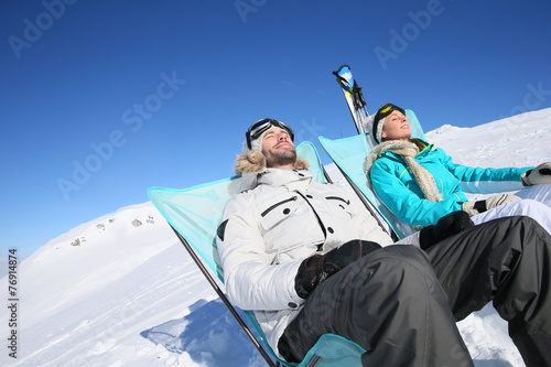Couple of skiers sunbathing at top of ski slope