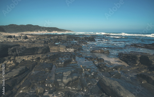 Dark rocks with blue sky at the wild coast of Morgans Bay. Easte