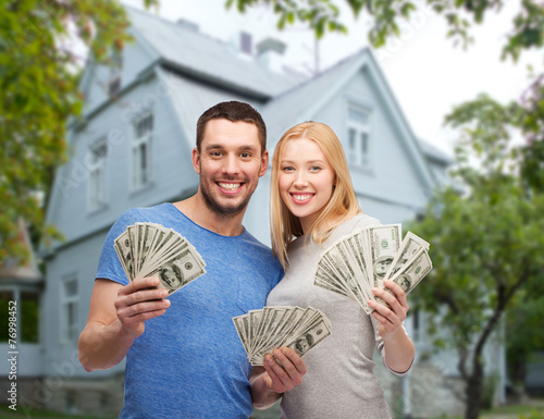 smiling couple showing money over house background