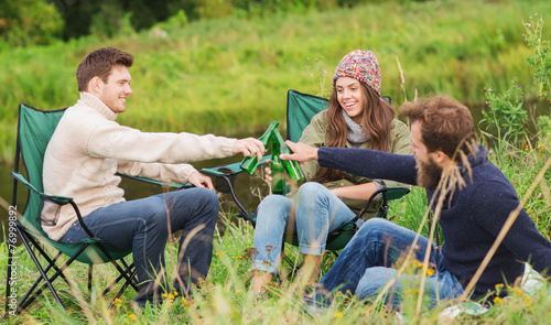 group of smiling tourists drinking beer in camping