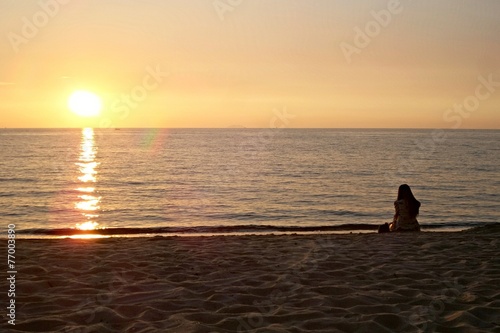 Girl sit alone on the beach to see sunset. © apitsada