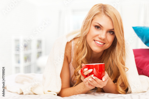 Young woman relaxing in bed with a cup of coffee