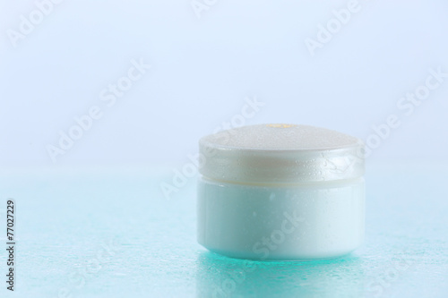 Cosmetic cream on blue background with water drops