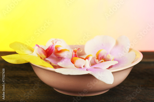 Bowl with orchids on table on bright background