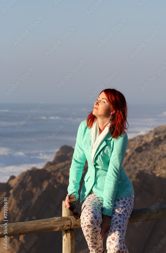 The young redhead woman enjoying sunlight at the seashore