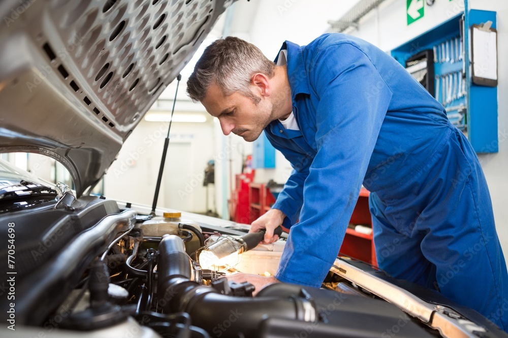 Mechanic examining under hood of car with torch Mechanic examining under hood of car with torch