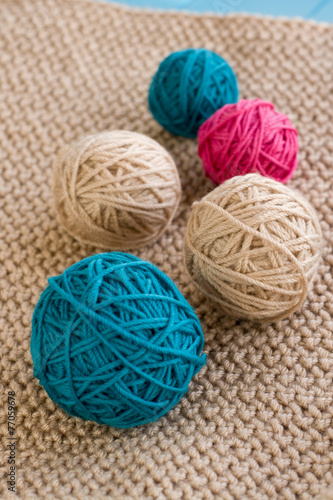 Bright balls of yarn lying on beige knitted plaid