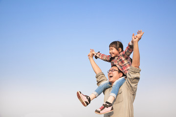 Father carrying his daughter on shoulders with blue sky backgrou