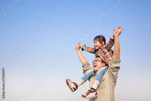 Father carrying his daughter on shoulders with blue sky backgrou