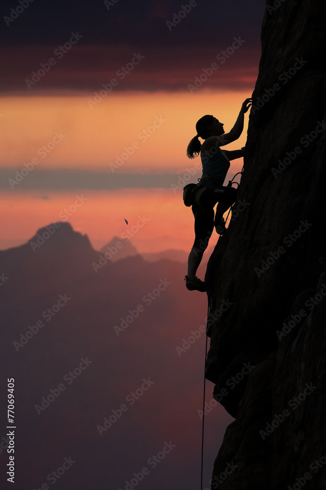 Elegant female alpine climber ascents rock against sunset