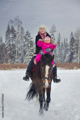 Mother and baby girl horseback riding at winter