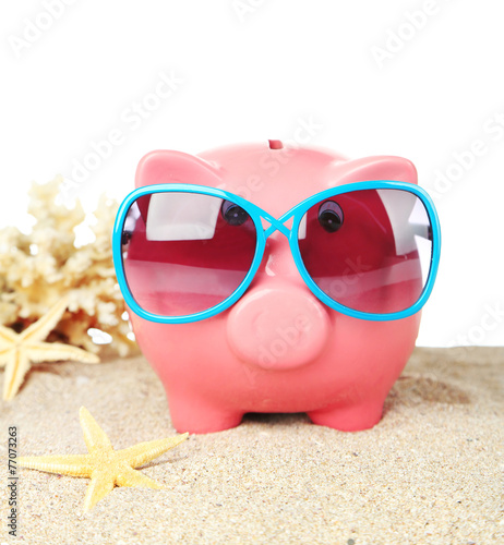 Piggy bank with sunglasses on sand, on white background