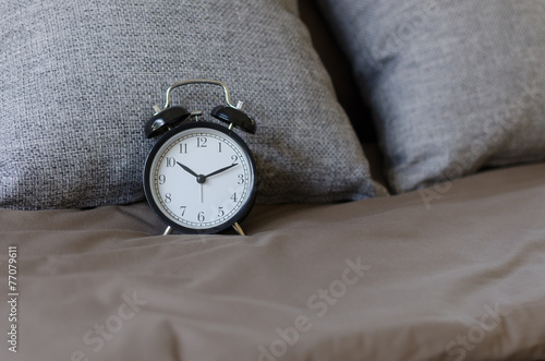black alarm clock on brown bed with grey pillow