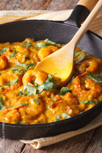 Prawns in curry sauce in a black frying pan close-up. vertical