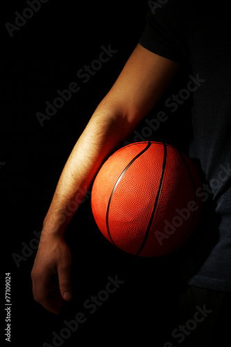 Basketball player holding ball, on dark background © Africa Studio