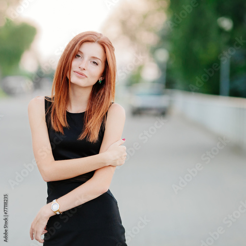 Cute young redhead woman in a black dress with a slight smile