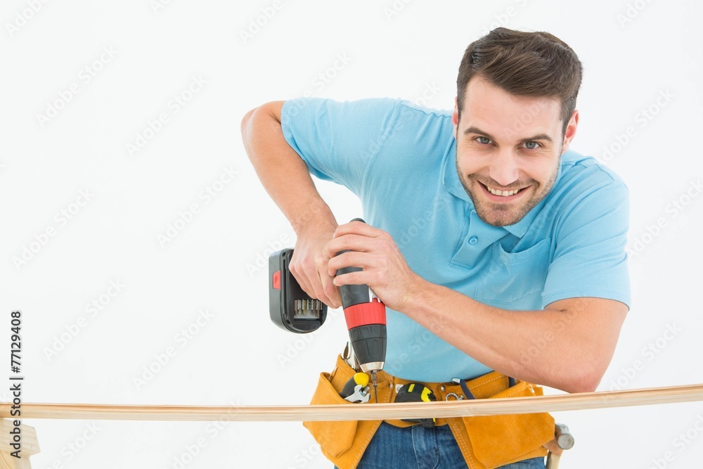 Smiling construction worker using hand drill on wooden plank Smiling construction worker using hand drill on wooden plank