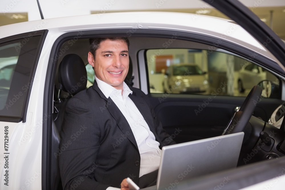 Smiling businessman using laptop in his car