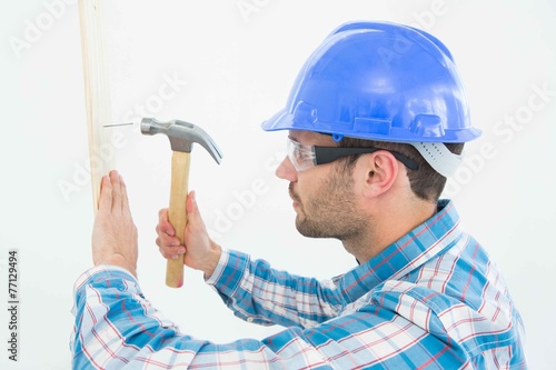 Fototapeta Carpenter hammering nail on wooden plank
