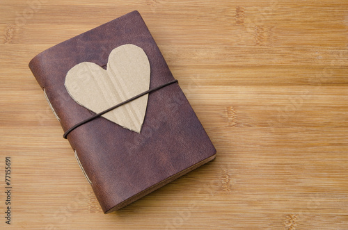 old notebook on a wooden table with a cardboard heart on top