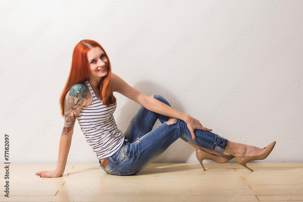 Laughing redhead woman with tattoo sitting on the floor