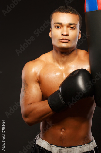 Handsome boxer posing with a punching bag on dark background